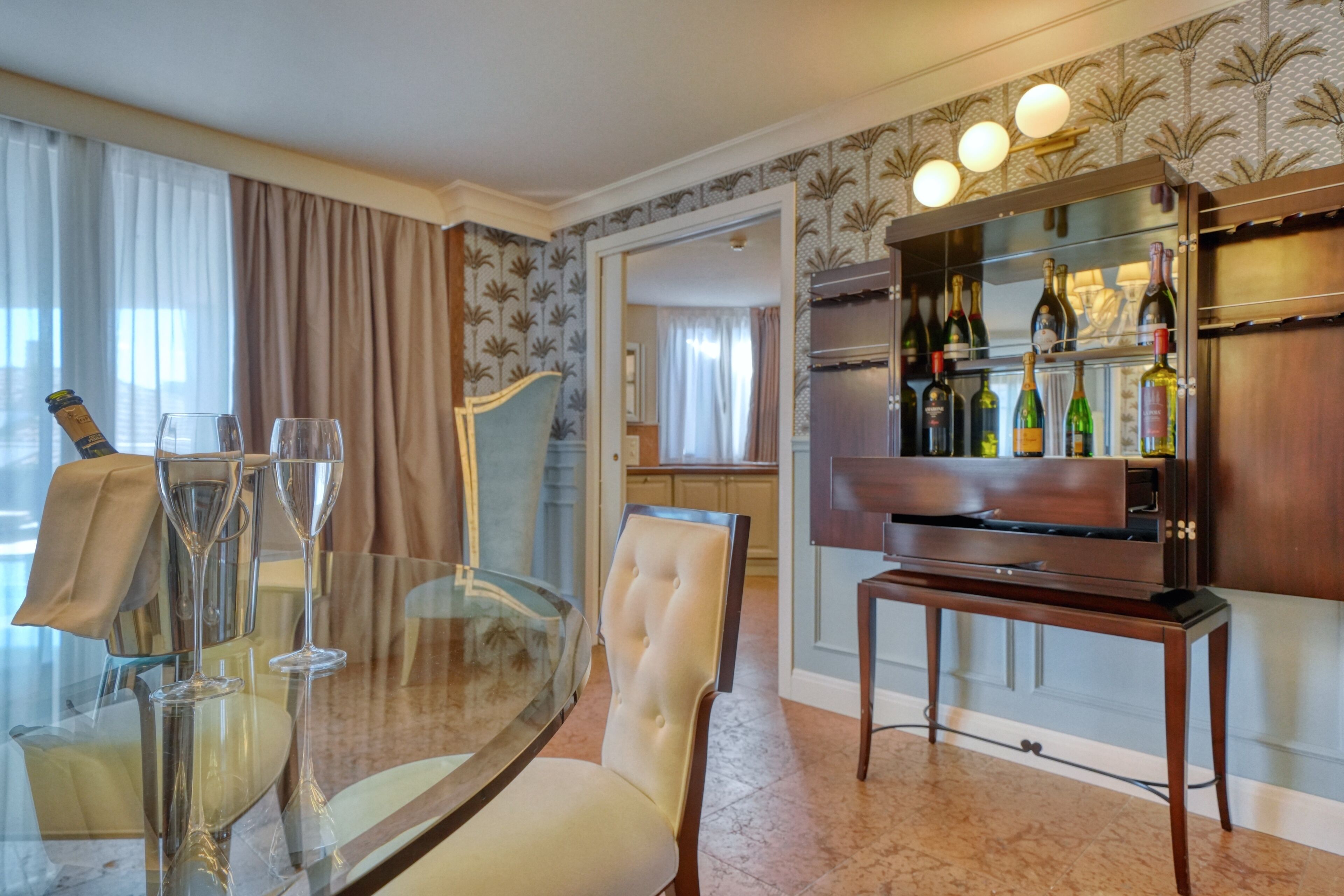 A dining area with a glass table, two chairs, and a wine rack with bottles.