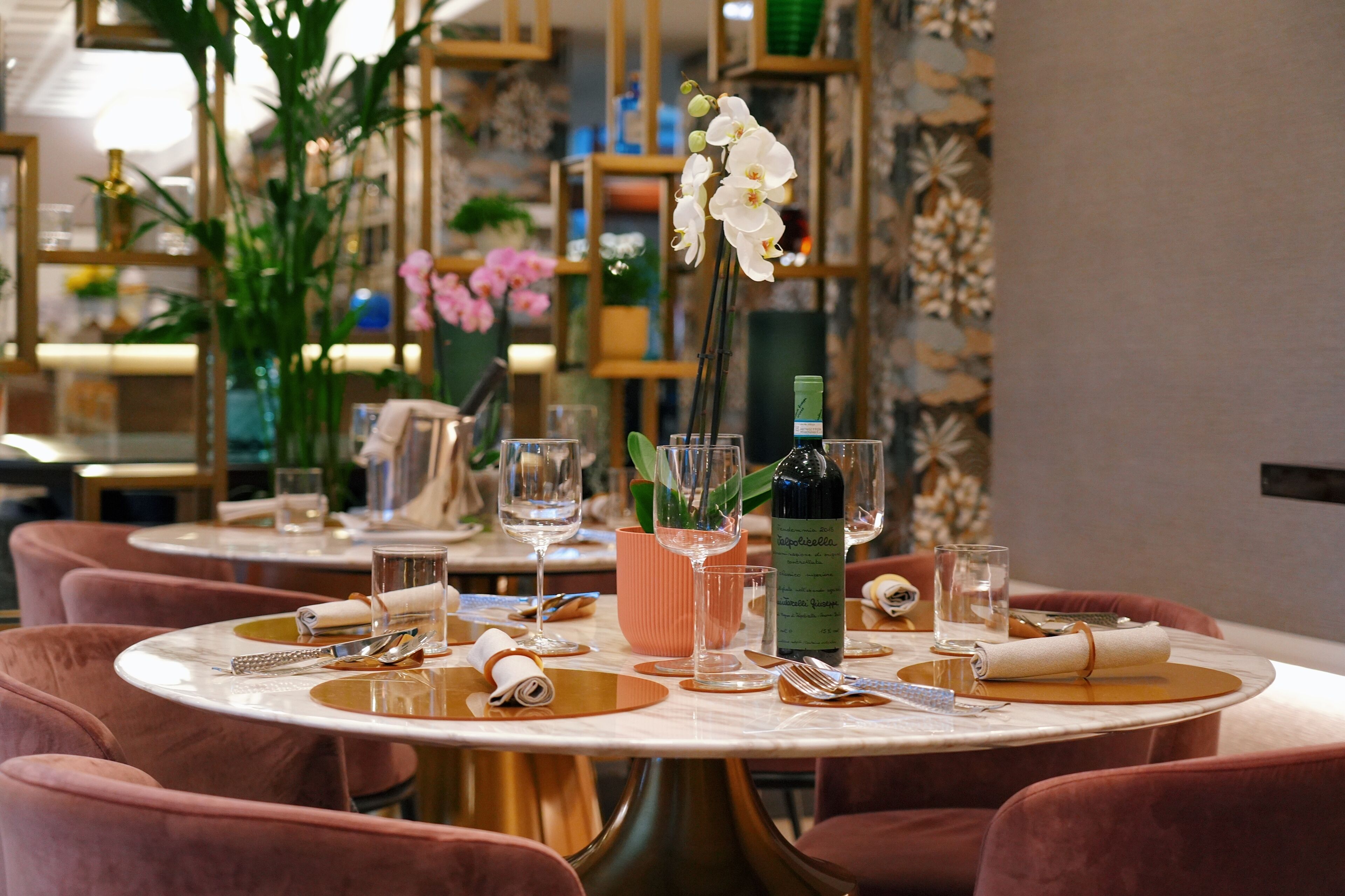 A dining area with round tables, pink upholstered chairs, and a vase with white orchids.