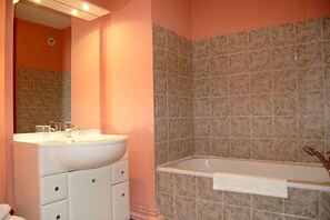 A bathroom with a white vanity, a large mirror, a bathtub, and a tiled wall. - Hôtel Domaine de Volkrange (Thionville)