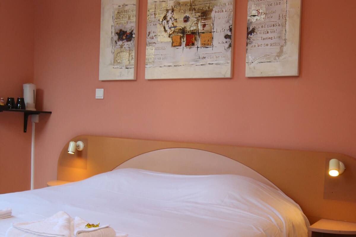 A neatly made bed with white linens and towels, a wooden headboard, and wall-mounted reading lamps.