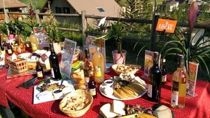 Ulkoilmassa oleva buffetpöytä, jossa on tarjolla erilaisia ruokia ja juomia, ja taustalla näkyy vehreää maisemaa ja talo.