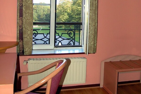 Una habitación con ventana que da a un jardín, un radiador, una silla de madera y una cama.
