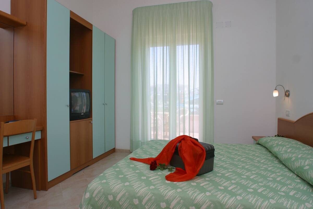 A bedroom with a bed, a desk, a wardrobe, and a window with curtains.
