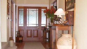 Un couloir avec un plancher en bois, un tapis, une porte avec des panneaux de verre, une lampe et un vase rempli de fleurs.