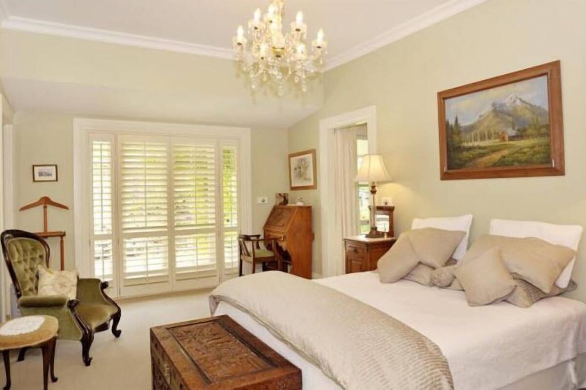 A bedroom with a large bed, a chandelier, a desk, and a chair.