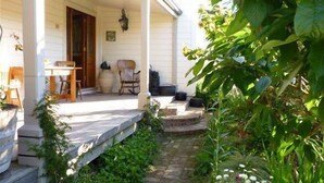 Un porche abrité avec une table et des chaises, une plante en pot et un chemin de pierres menant à une porte.