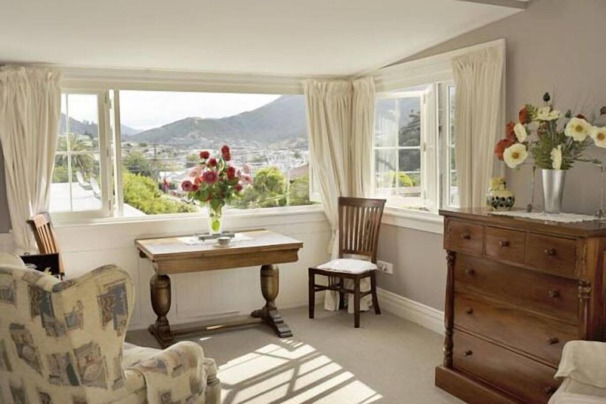 A room with a large window, a wooden desk, a chair, and a dresser.