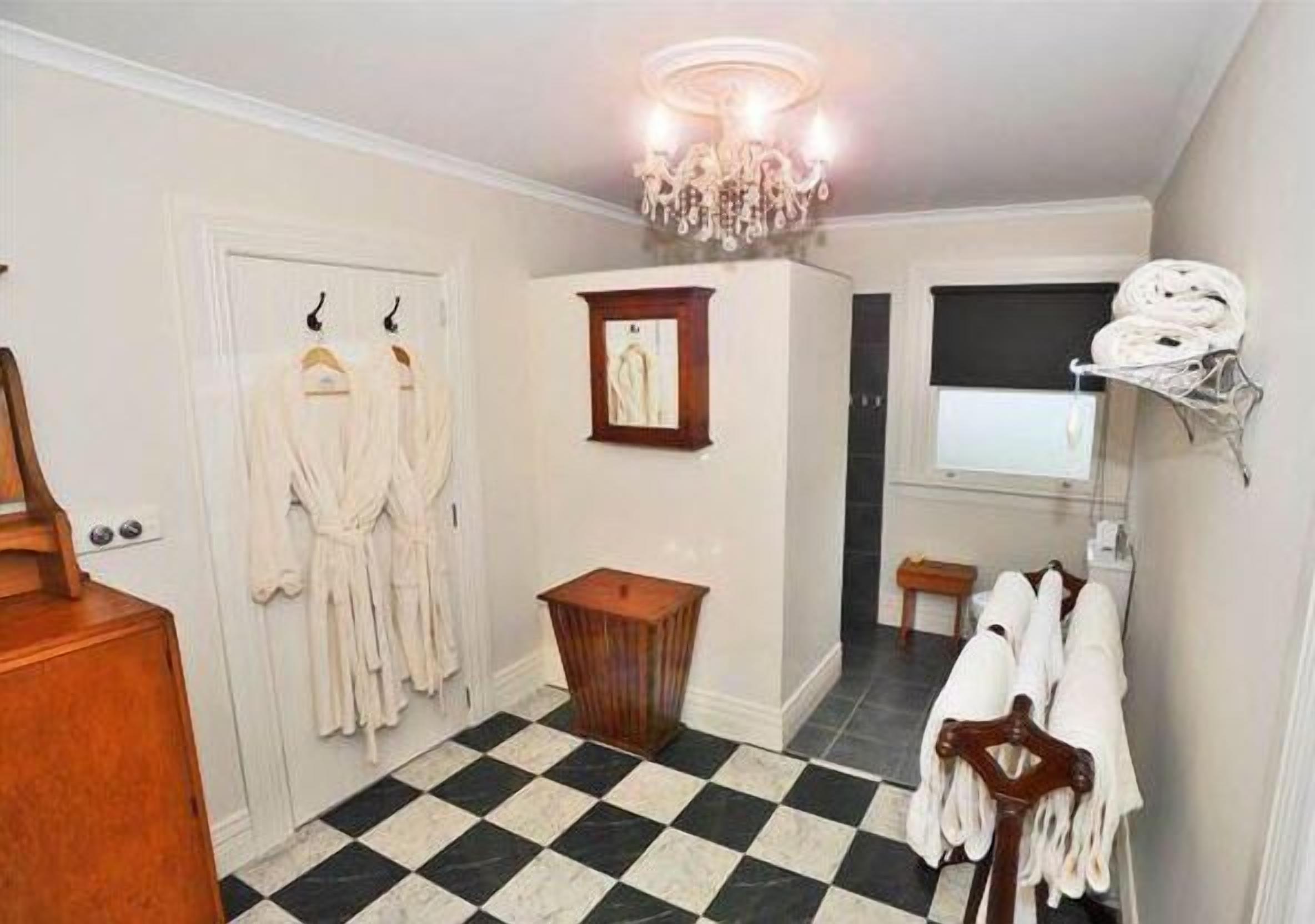 A hotel room with a checkered floor, a chandelier, a wooden cabinet, and a rack with robes.