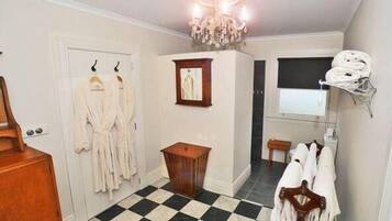 A hotel room with a checkered floor, a chandelier, a wooden cabinet, and a rack with robes.