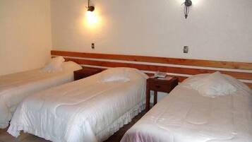 Quarto de hotel com três camas de solteiro, cabeceiras de madeira e luminárias fixadas na parede.
