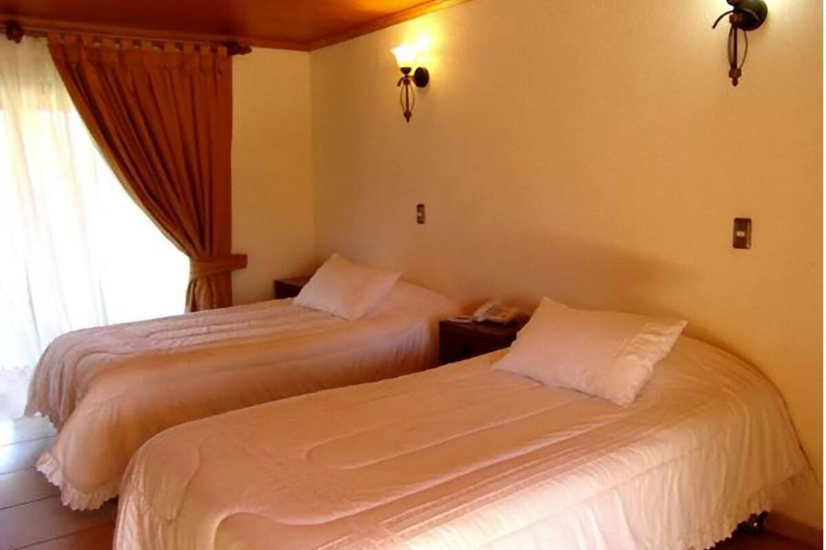 Two single beds with white linens, a wooden headboard, a nightstand with a telephone, and wall-mounted lighting.