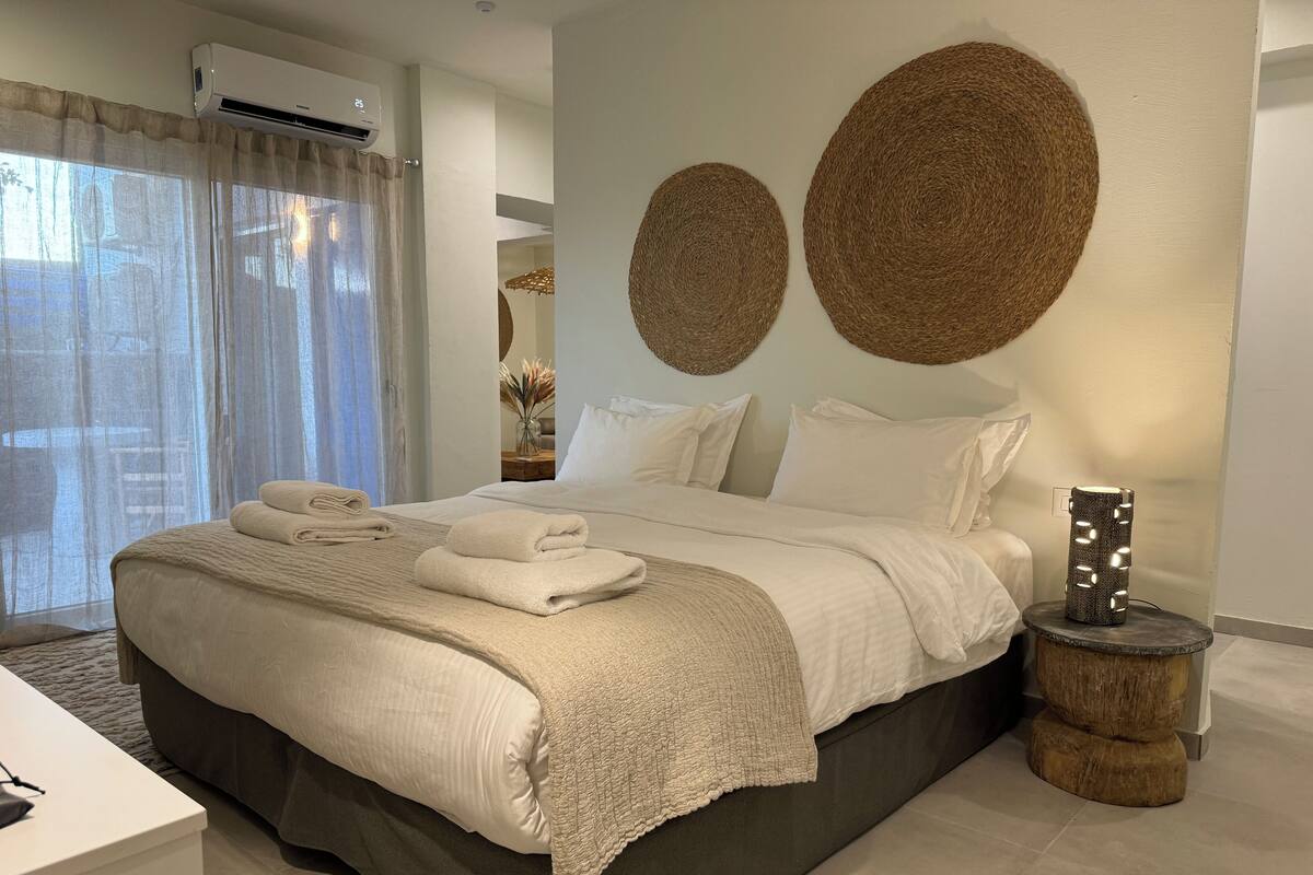 Quarto moderno com uma cama grande, uma mesa de cabeceira, ar condicionado na parede e um detalhe decorativo na parede.