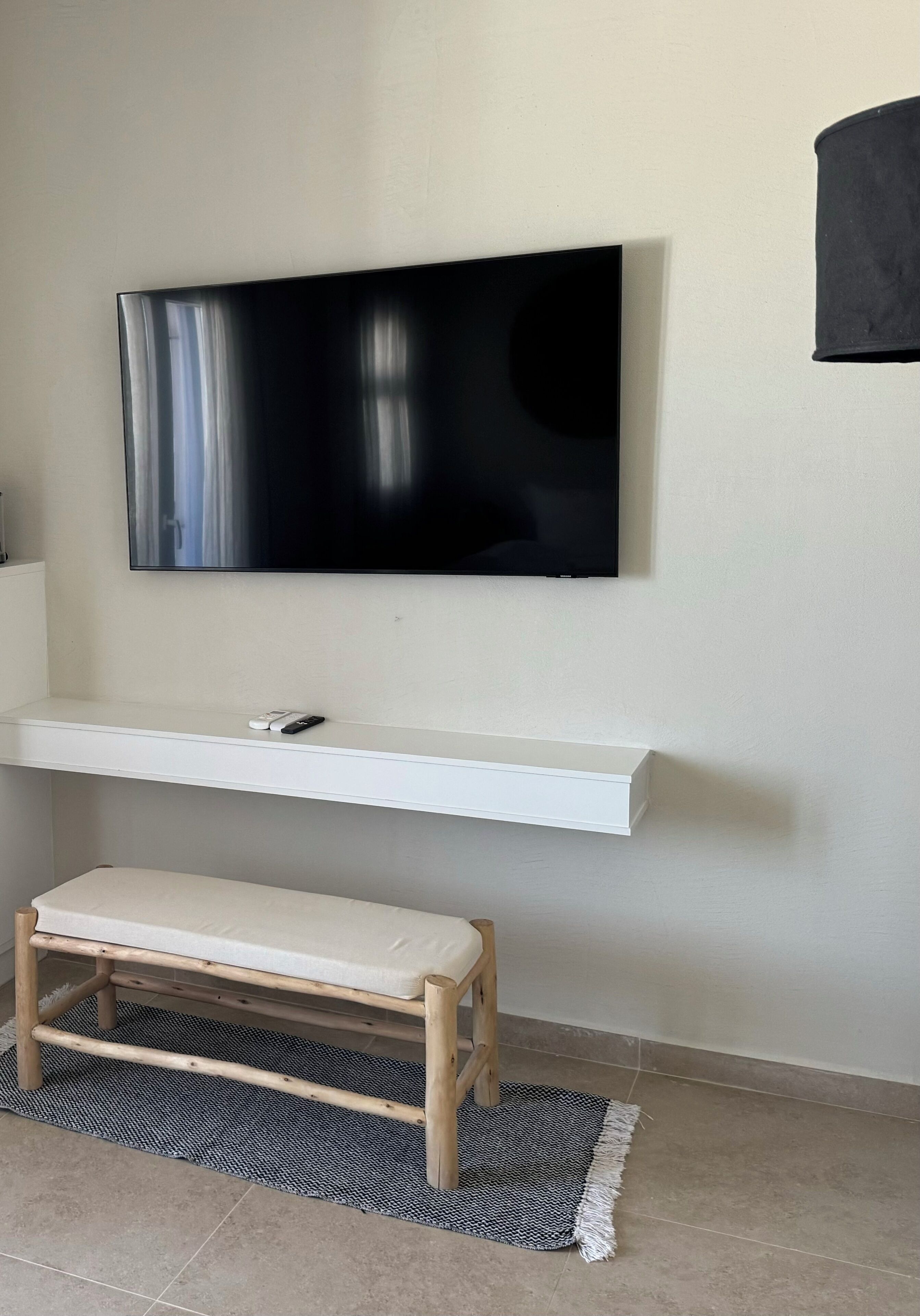 A modern living room with a flat-screen TV mounted on a white wall, a wooden bench, and a patterned rug.