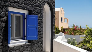 A stone wall with a blue door and window, a white balcony, and a building with a beige facade in the background.