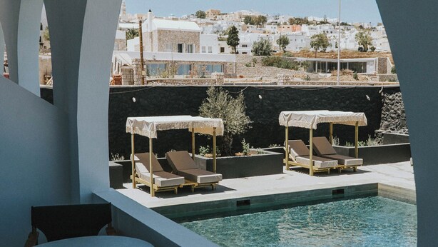 A poolside area with lounge chairs and umbrellas, a clear view of a coastal town in the background.