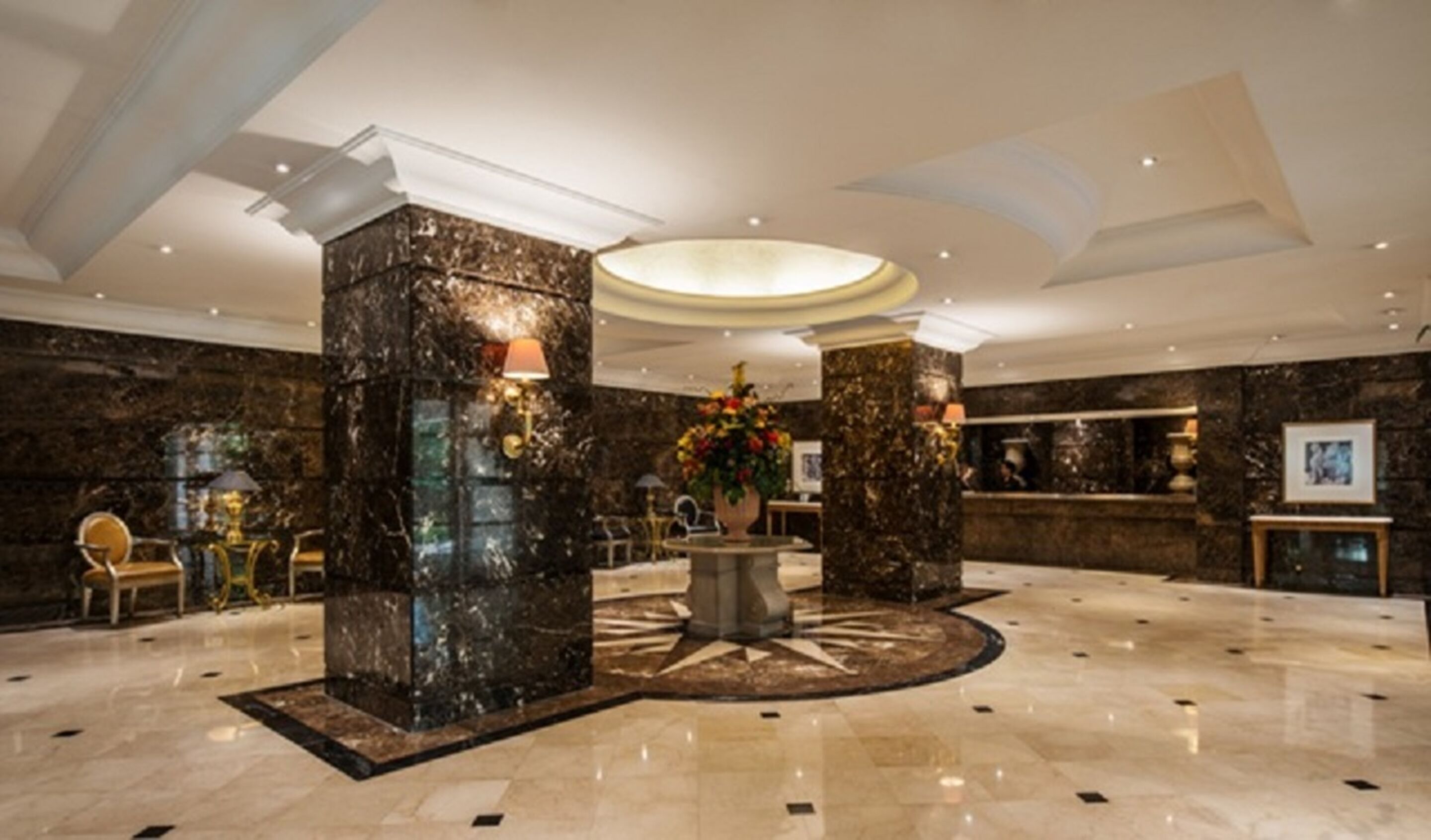 Un hall d’entrée spacieux, orné de colonnes en marbre, avec une grande table ronde au centre et un imposant arrangement floral.