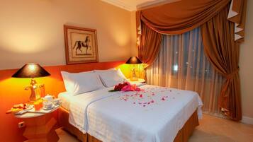 A hotel room with a bed, two bedside lamps, a framed picture on the wall, and a window with curtains.