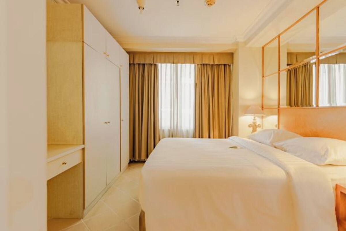 A hotel room with a bed, a wardrobe, a mirror, and curtains.