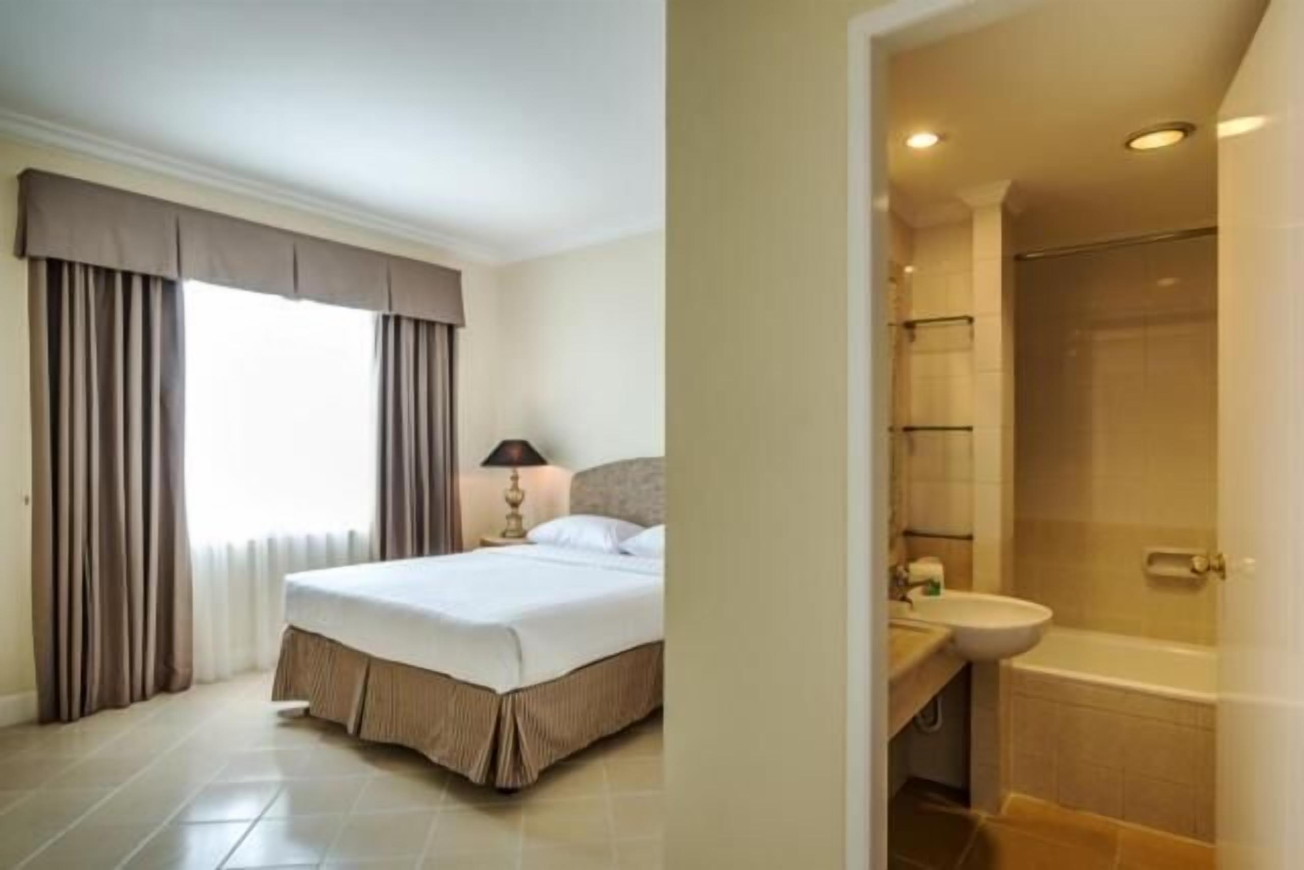 A hotel room with a bed, a nightstand, a lamp, a bathroom with a sink and a bathtub.