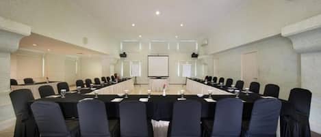 Un salón de conferencias con una larga mesa, sillas y una pantalla para proyector.