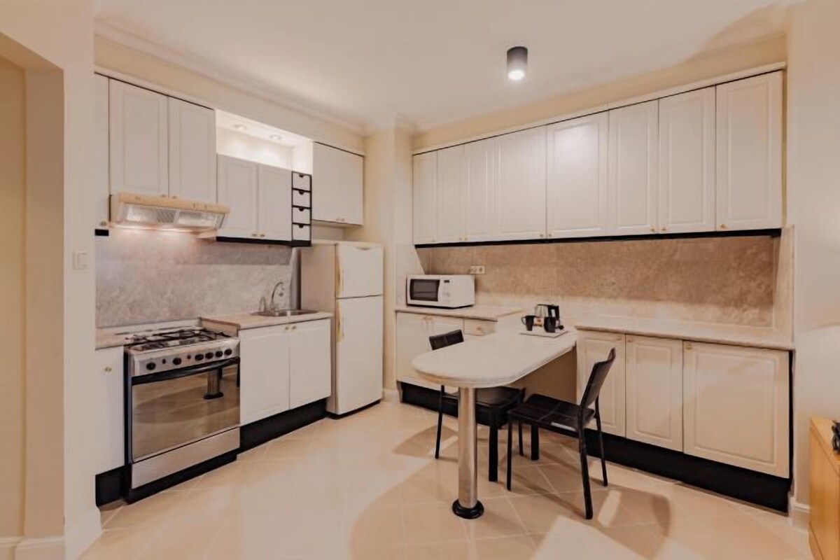 Une cuisine moderne avec des meubles blancs, une cuisinière, un four à micro-ondes et un coin repas comprenant une table et des chaises.