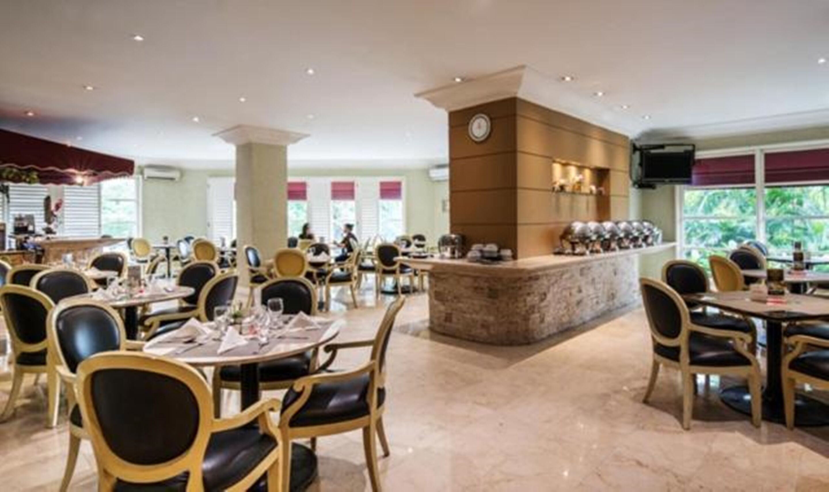 A restaurant with round tables and chairs, a central bar area, and large windows.