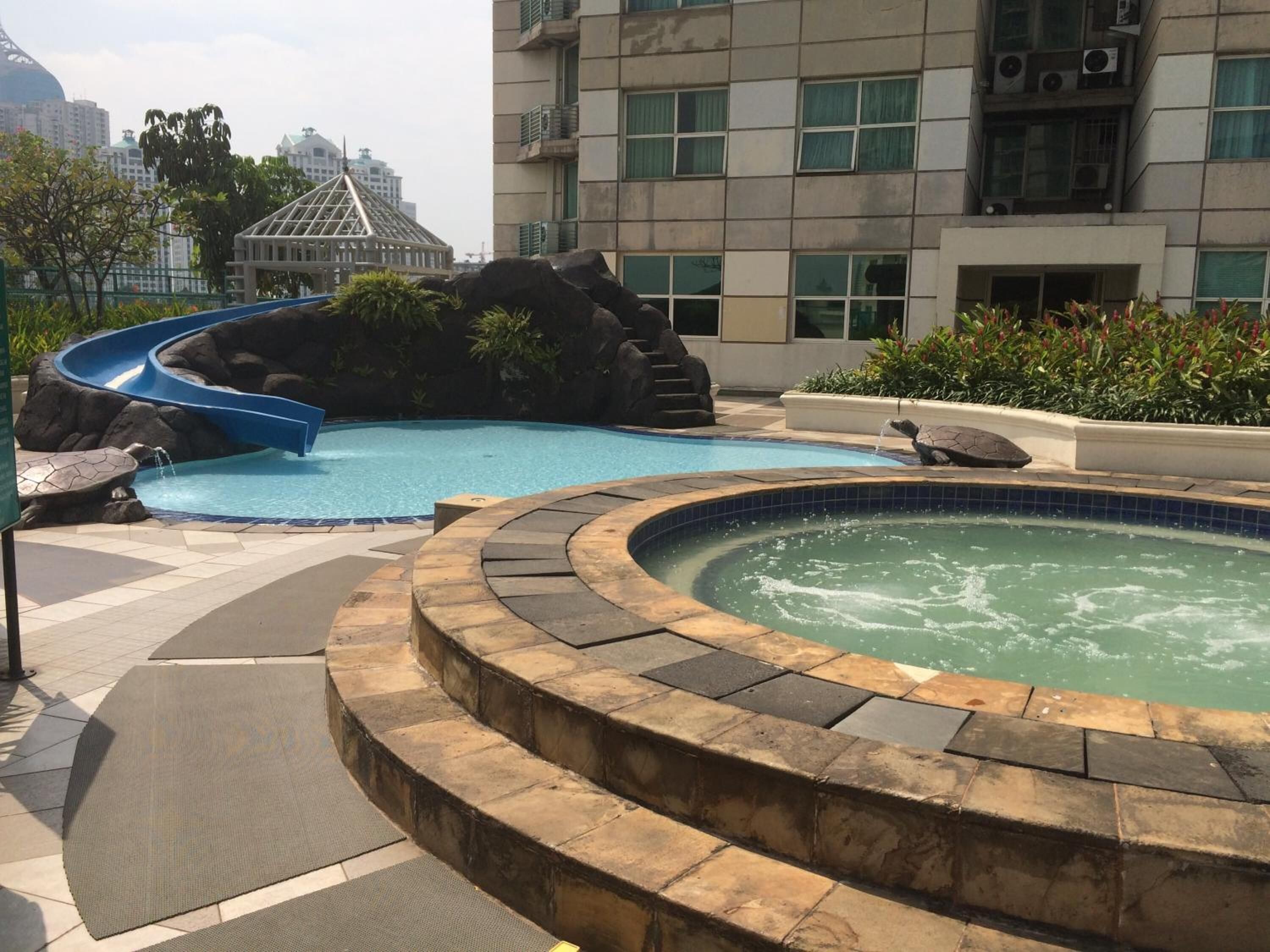 Une piscine avec un toboggan, un jacuzzi et un élément décoratif en roche.