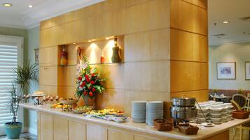 A buffet setup with various dishes, a vase of flowers, and a coffee station.