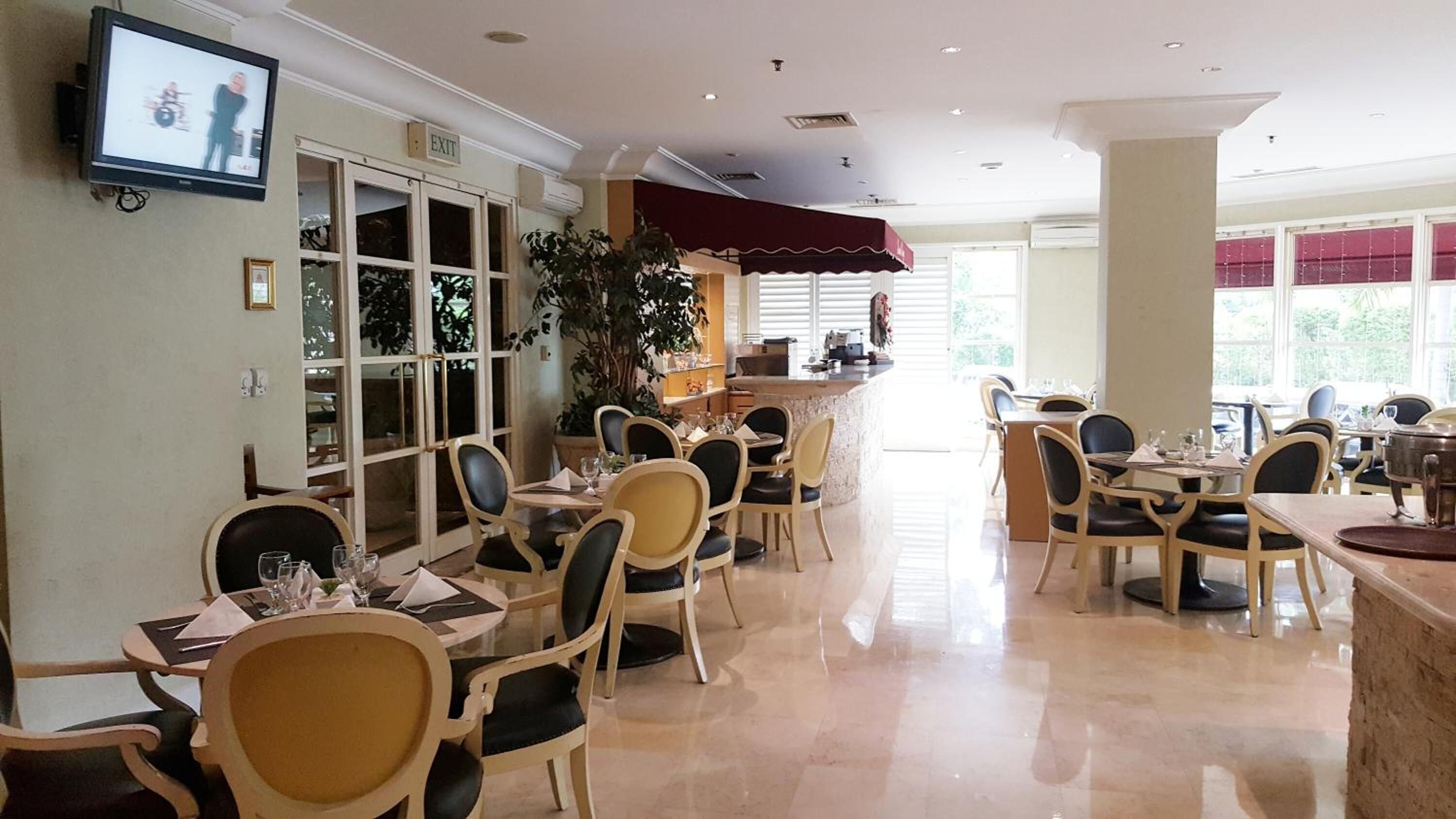 Uma sala de jantar ampla com várias mesas e cadeiras, um espaço de bar e uma televisão na parede.