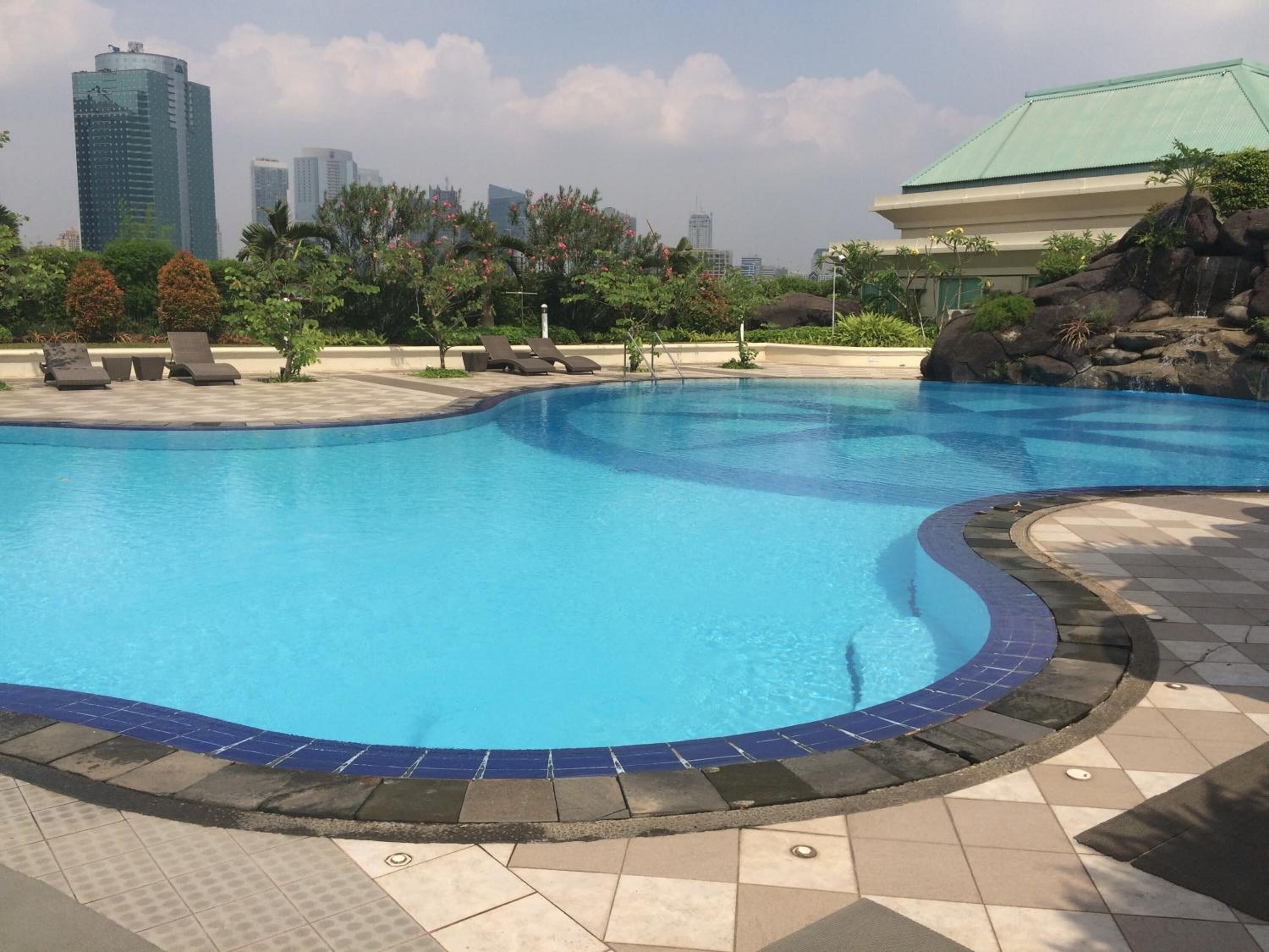 A swimming pool with a tiled edge, lounge chairs, and a cityscape in the background.