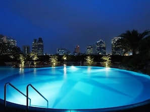 Une piscine offrant une vue sur les toits de la ville illuminée la nuit.