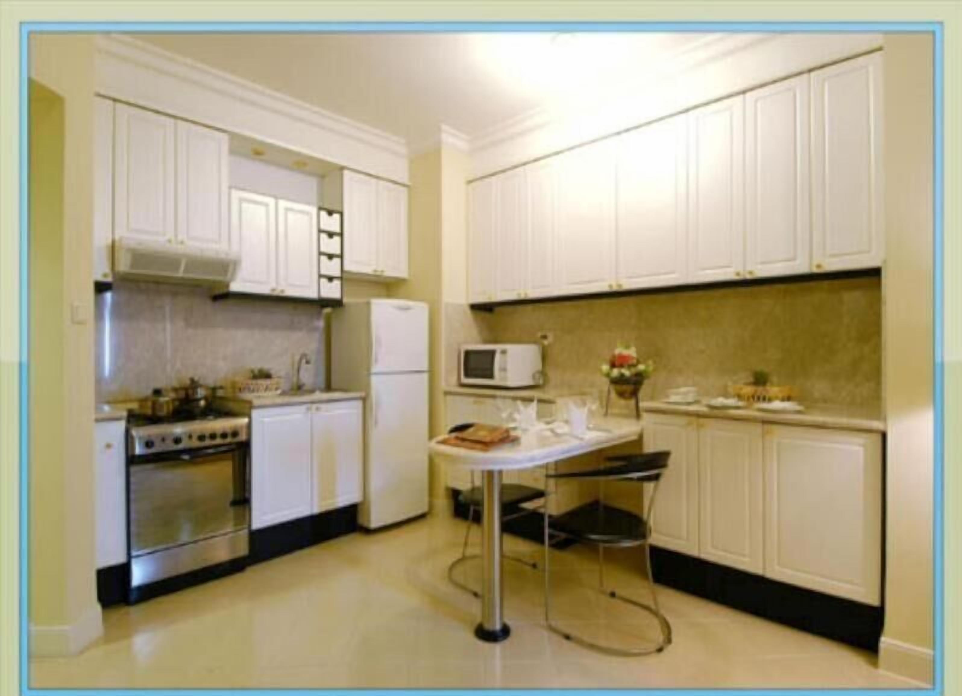 Uma cozinha compacta com armários brancos, fogão, micro-ondas e uma pequena mesa de jantar com cadeiras.