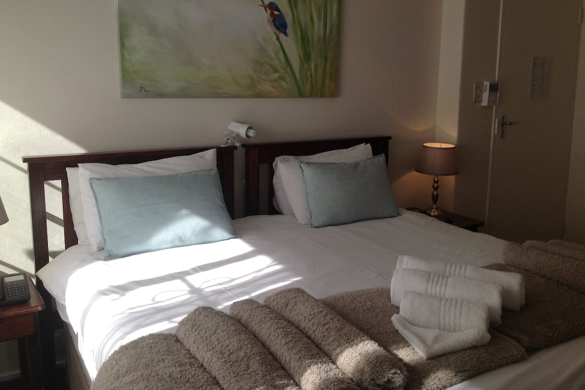 Ein Hotelzimmer mit Bett, Kissen, einer Lampe, einem Gemälde und Handtüchern.