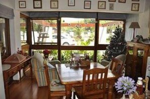 Un coin repas avec une table et des chaises en bois, un sapin de Noël et une vue sur l’extérieur.
