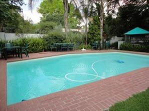 Une piscine bordée de briques, entourée de verdure et agrémentée de mobilier d’extérieur.