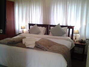 A hotel room with a large bed, two bedside lamps, a wooden headboard, and a nightstand with a phone and a lamp. - Crane's Nest Guest House at 212 (Pretoria)