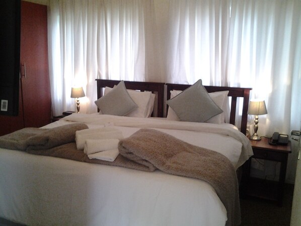 A hotel room with a large bed, two bedside lamps, a wooden headboard, and a nightstand with a phone and a lamp. - Crane's Nest Guest House at 212 (Pretoria)