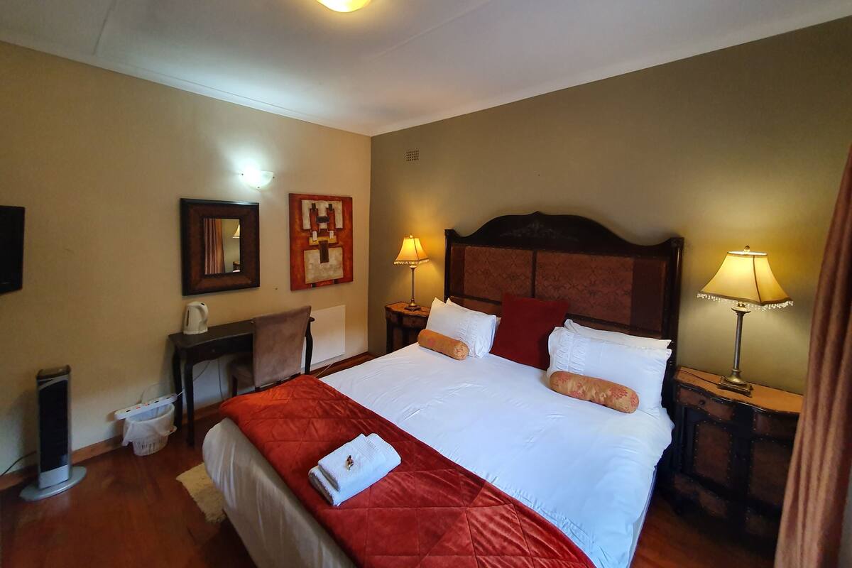 Habitación de hotel con una cama grande, dos lámparas de noche, una mesita de noche, un espejo y una obra de arte en la pared.
