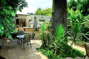 A patio area with a table and chairs, surrounded by lush greenery and a tree.