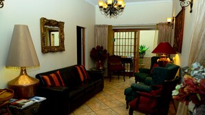 Un salon comprenant un canapé, des fauteuils, une lampe, un miroir et un coin repas avec une table et des chaises.