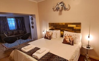 A hotel room with a bed, a sofa, a dining area, and a view of the outdoors.