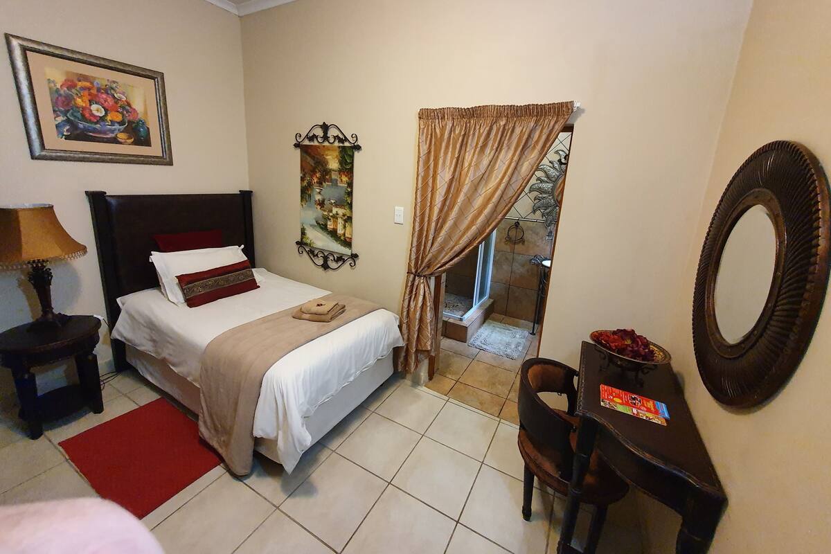 Habitación de hotel con cama, escritorio, silla, lámpara, un cuadro, espejo y zona de ducha.