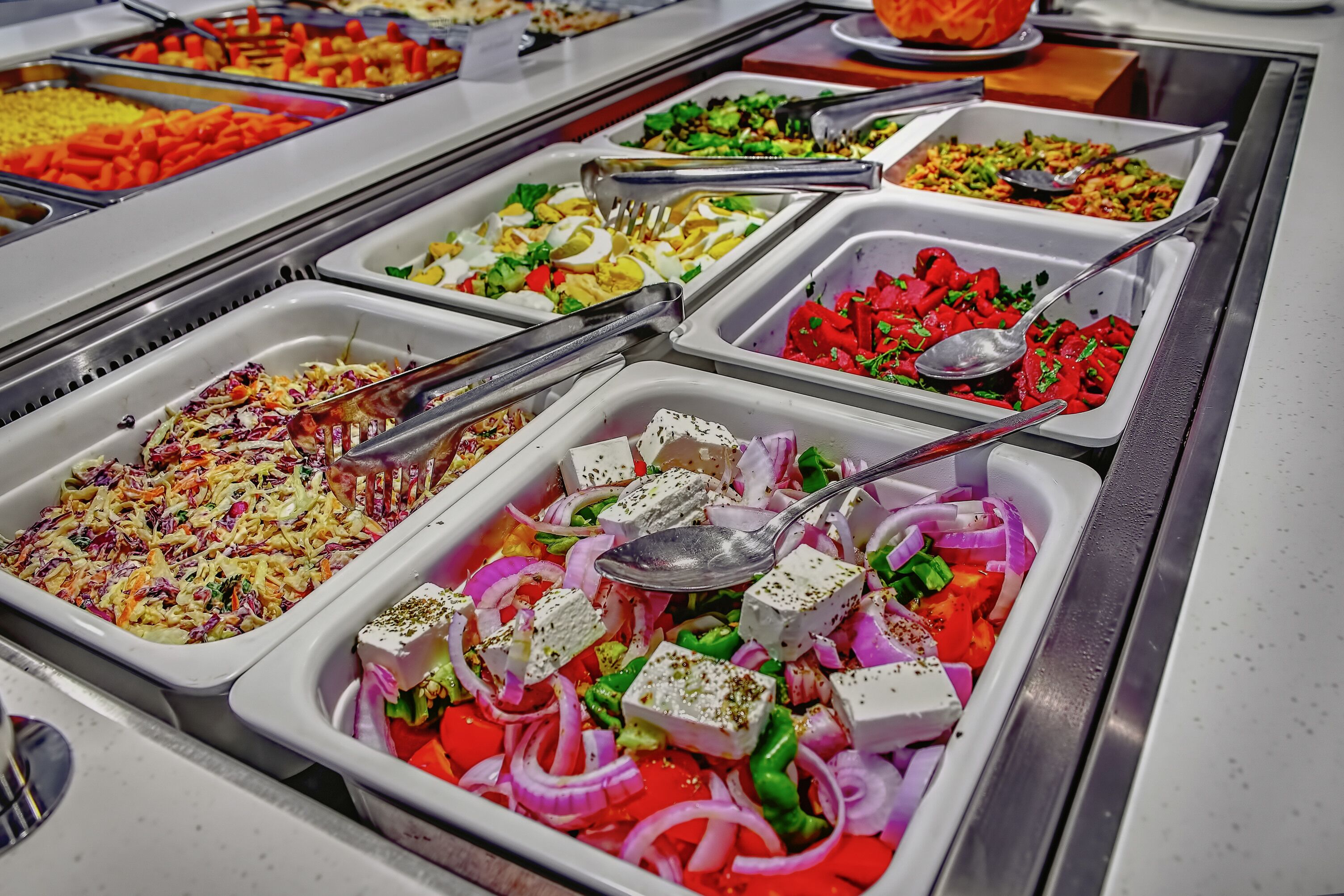 A buffet with various dishes including coleslaw, feta cheese, and mixed vegetables.