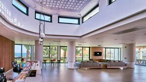 Un vestíbulo moderno y espacioso, con techo alto, ventanas grandes y una zona de estar con sofás y sillones.