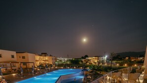Vista nocturna de un área de piscina con sillones de descanso y barandilla de vidrio con vistas a la piscina.