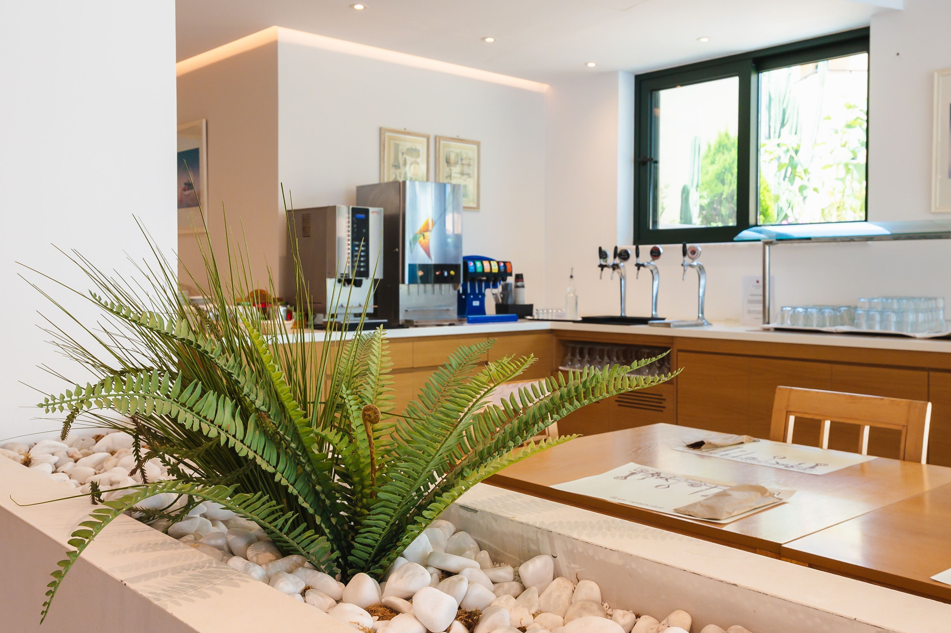 A modern kitchen with a central island, a coffee machine, and a window with a view of greenery.