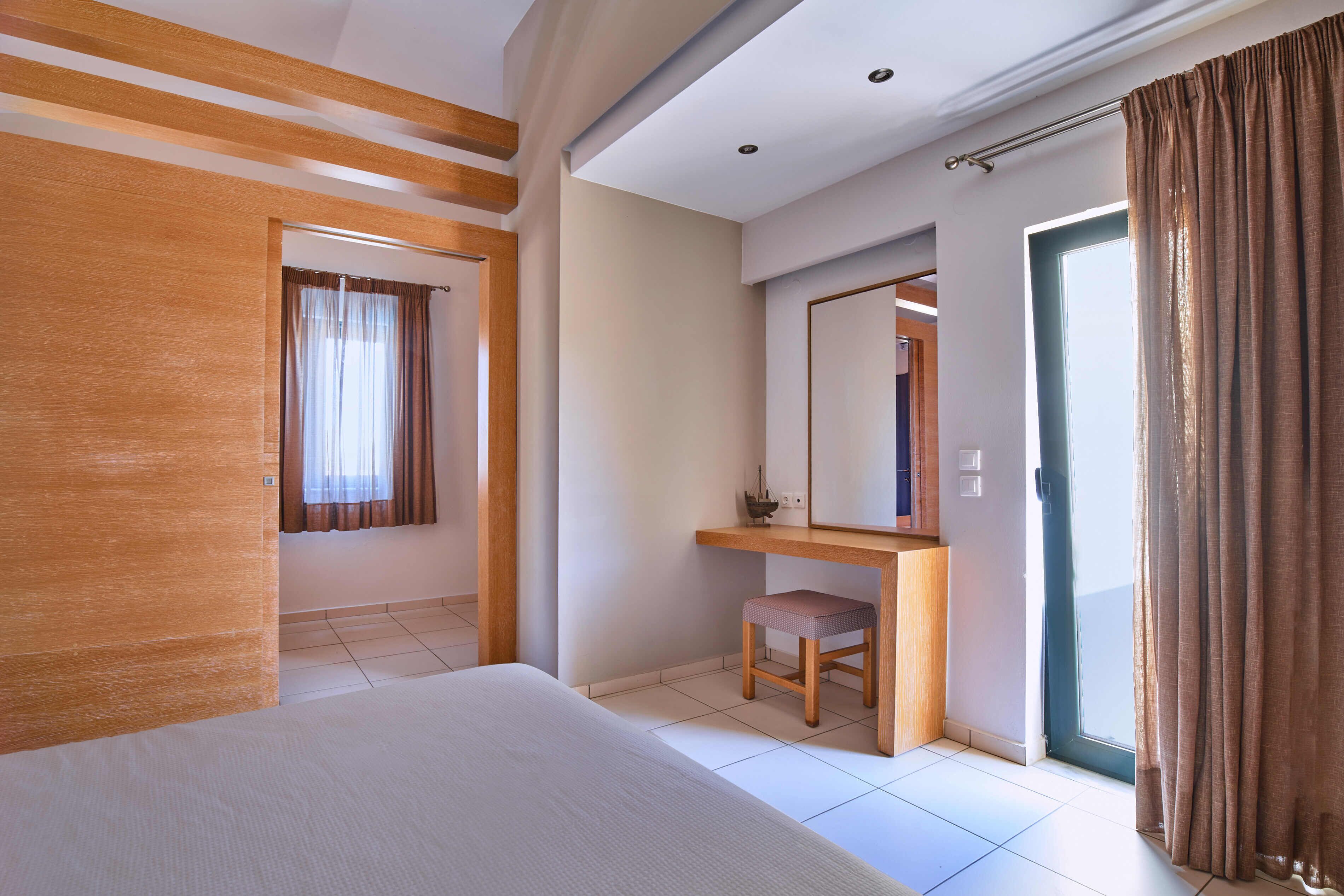 A hotel room with a bed, a desk, a chair, a mirror, and a door.