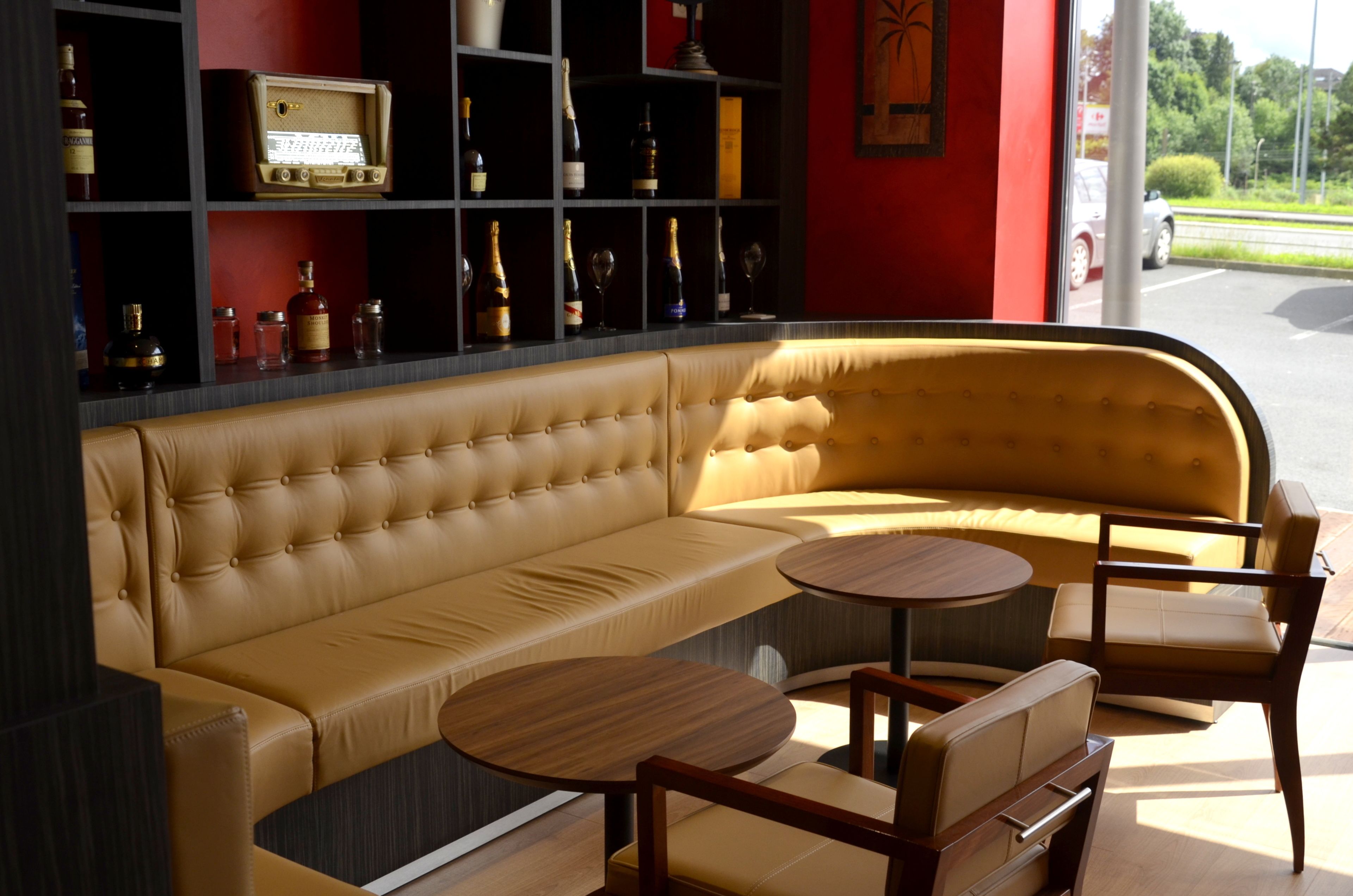 A modern lounge with a curved sofa, wooden side tables, and a wine and liquor display.