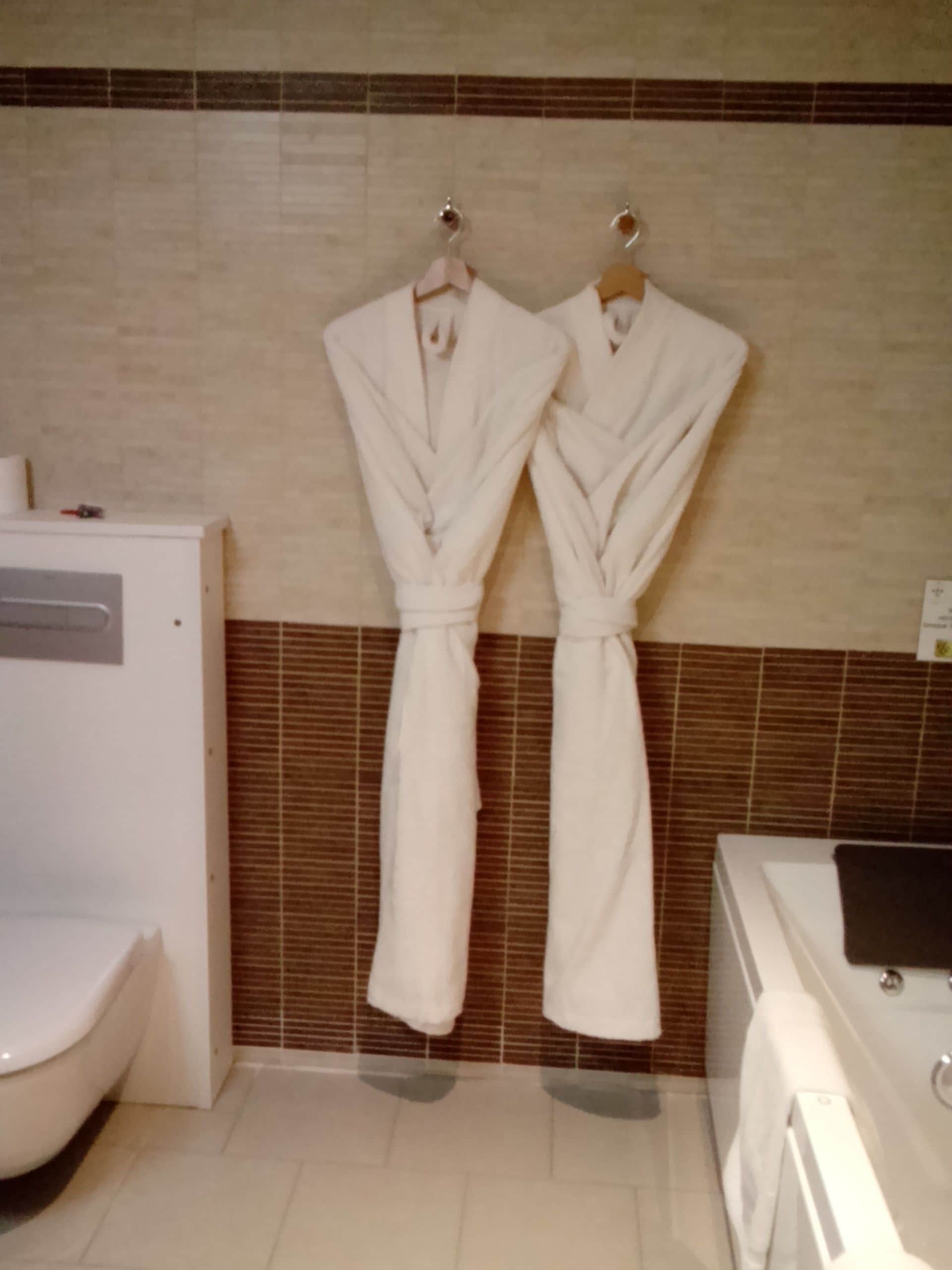 A bathroom with two white robes hanging on hooks, a toilet, and a bathtub.