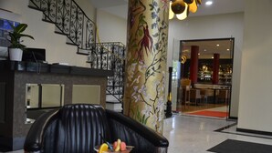 Um hall com poltrona de couro preto, um copo de drink, escada com grades ornamentadas e um pilar com motivos florais.